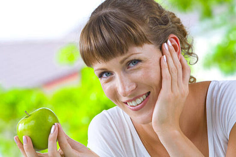 Lächelnde junge Frau mit einem grünen Apfel in der Hand