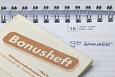 Ein Bonusheft liegt auf einem aufgeschlagenen Tischkalender Ein Bonusheft liegt auf einem aufgeschlagenen Tischkalender