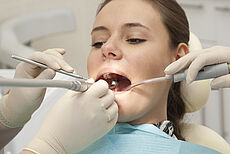 Junge Frau auf dem Zahnarztstuhl während einer Zahnbehandlung mit Sonde und Absauger