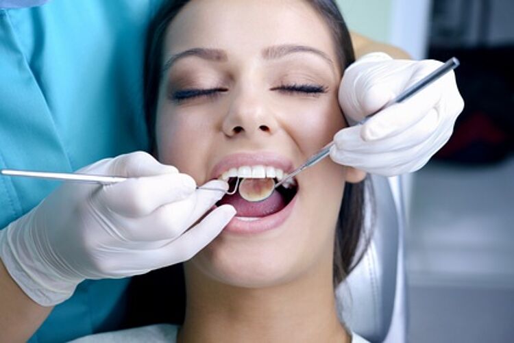 Junge Frau und zwei behandschuhte Hände mit Sonde und Spiegel bei einer Zahnarztbehandlung